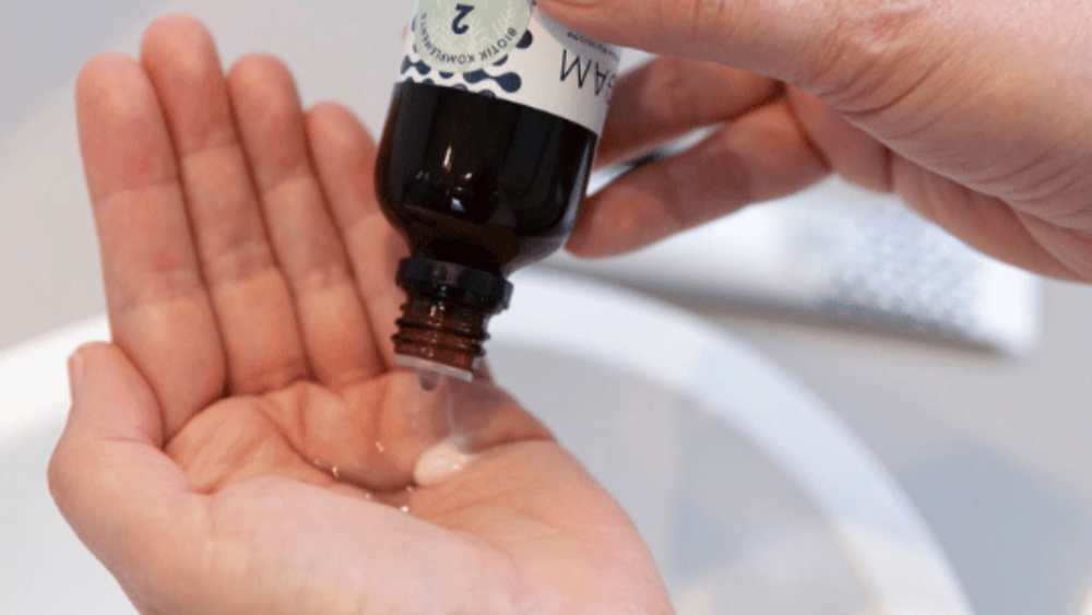 Person holding a small bottle with a dropper over their palm, dispensing a liquid.